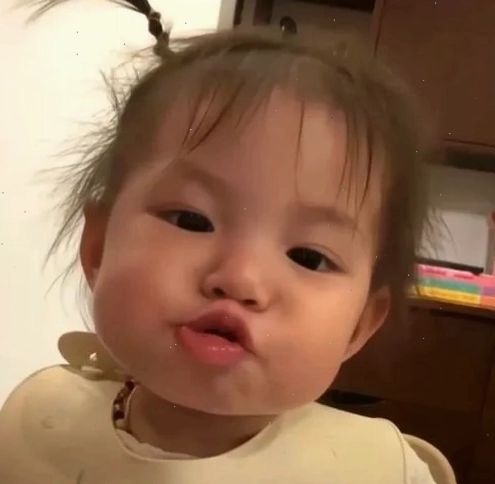 Bé gái bụ bẫm buộc tóc hai bên làm trò bặm môi trợn mắt trước ống kính, tạo nét nghịch ngợm